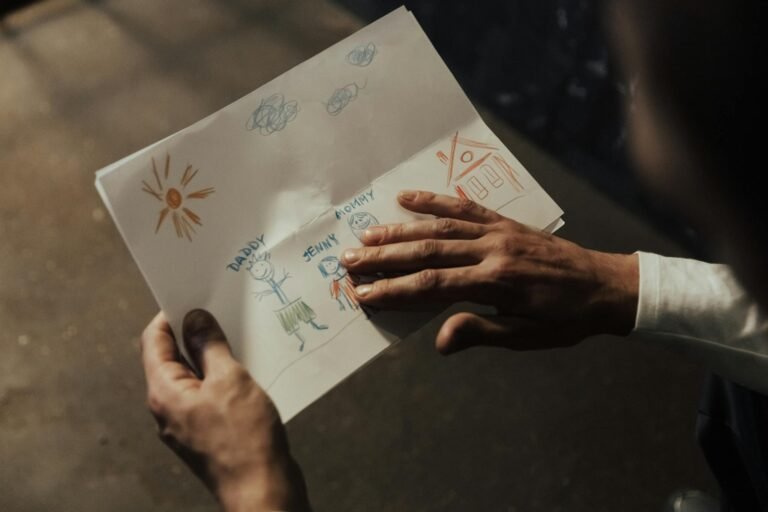 Close-up of a person's hands holding a child's drawing depicting a family scene.