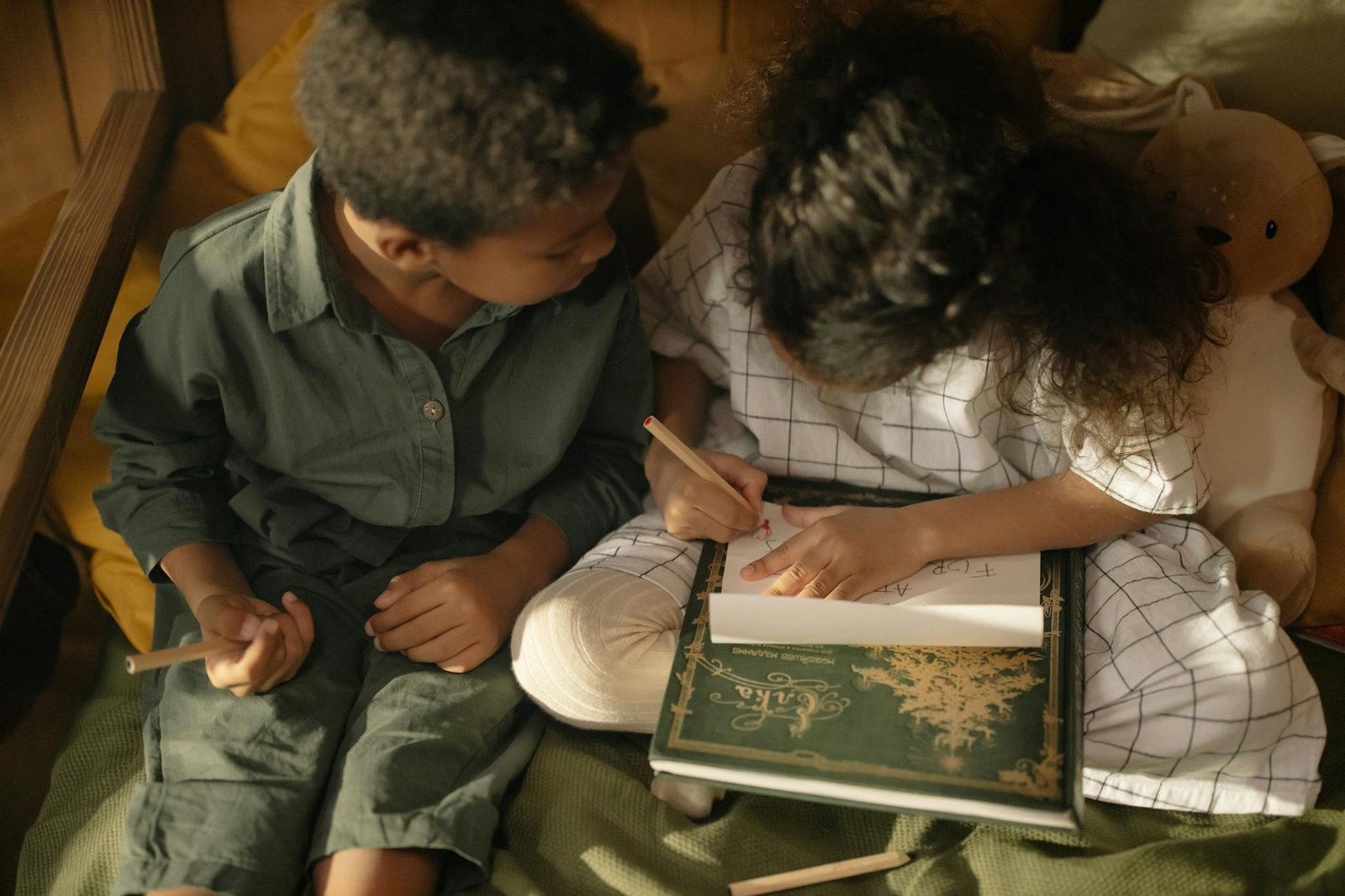 Two children sitting indoors, drawing together in a cozy setting.